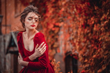 Portrait of Beautiful girl in a burgundy and red dress on a background of autumn grape leaves in the park, October