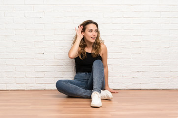 Young blonde woman sitting on the floor listening something