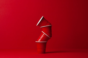red plastic glasses stacked in a stack on a red background, the concept of pollution, an increase...