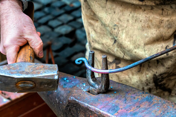 Blacksmith is processing a hot metal object at anvil in a workshop