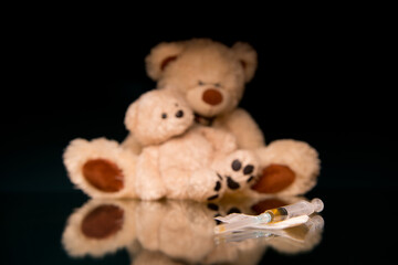 syringe with a dose of drugs and teddy bears in defocus