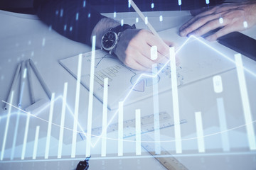 Double exposure of man's hands writing notes of stock market with forex chart.
