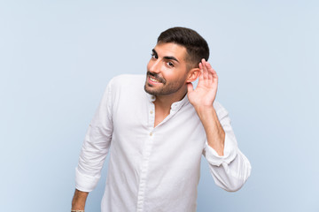 Handsome man with beard over isolated blue background listening to something by putting hand on the ear