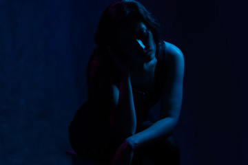 Obraz premium studio portrait of a girl in the light of blue and magenta neon lights. sad sits on a chair