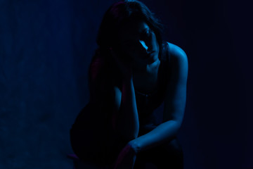 studio portrait of a girl in the light of blue and magenta neon lights. sad sits on a chair