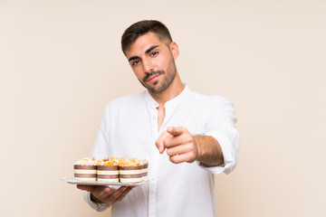 Handsome man holding muffin cake over isolated background points finger at you with a confident expression
