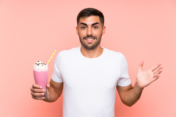 Young man with strawberry milkshake over isolated pink background with shocked facial expression