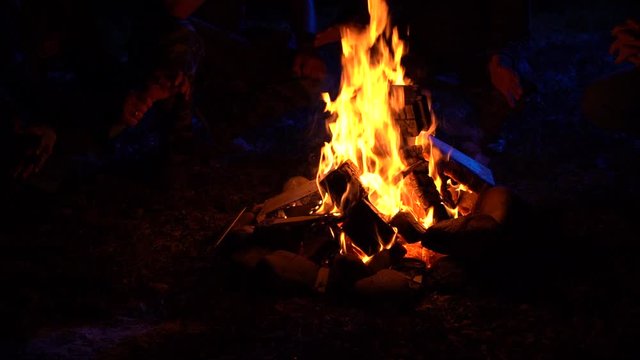 Four men sit near the fire at night in moonlight warm their hands and tell scary stories 100 fps Slow Motion