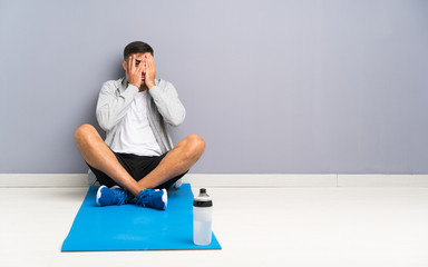 Sport man sitting one the floor covering eyes and looking through fingers