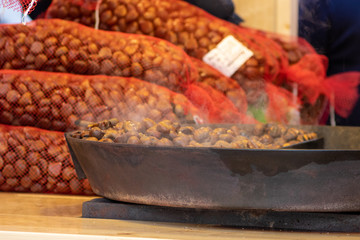 Mann bereitet frische heiße Maronen auf einem Marktstand eines Weihnachtsmarktes in der Adventszeit zu und bietet duftende Leckereien mit Esskastanien in einer großen Pfanne an