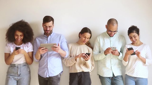 Multiracial smiling young people group using gadgets standing in row