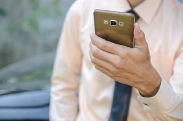 Businessman holds mobile phone near car