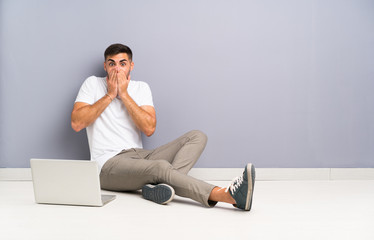 Young man with his laptop sitting one the floor with surprise facial expression