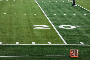 Obraz premium View of 20 yard line markers for American football field with feet of person standing on artificial turf