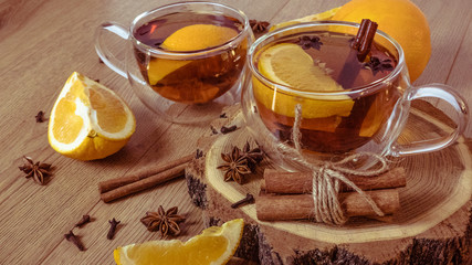 Orange flavored tea with cinnamon and cardamom in glasses, orange and cinnamon sticks on a wooden table. Mulled wine and spices on wooden background. Selective focus. Close up.