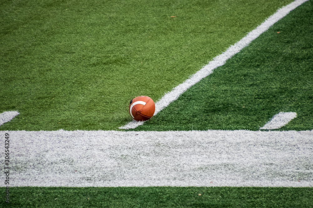 Wall mural football sitting on artificial turf of american football feld in anticipation of game