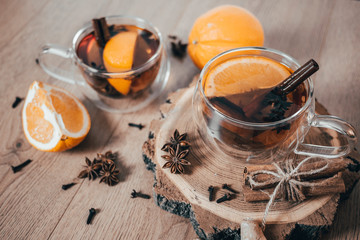 Orange flavored tea with cinnamon and cardamom in glasses, orange and cinnamon sticks on a wooden table. Mulled wine and spices on wooden background. Selective focus. Close up.