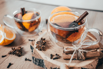 Orange flavored tea with cinnamon and cardamom in glasses, orange and cinnamon sticks on a wooden table. Mulled wine and spices on wooden background. Selective focus. Close up.