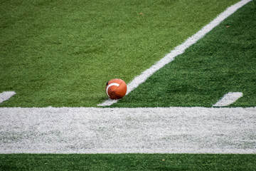 Football sitting on artificial turf of American football feld in anticipation of game