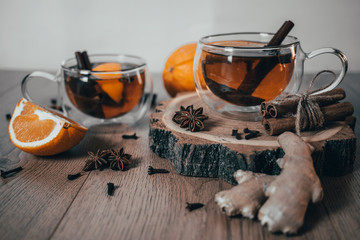 Orange flavored tea with cinnamon and cardamom in glasses, orange and cinnamon sticks on a wooden table. Mulled wine and spices on wooden background. Selective focus. Close up.