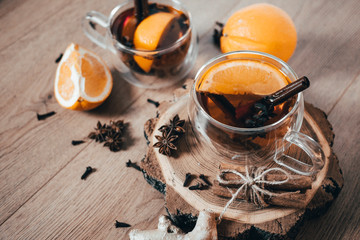 Obraz na płótnie Canvas Orange flavored tea with cinnamon and cardamom in glasses, orange and cinnamon sticks on a wooden table. Mulled wine and spices on wooden background. Selective focus. Close up.