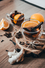 Orange flavored tea with cinnamon and cardamom in glasses, orange and cinnamon sticks on a wooden table. Mulled wine and spices on wooden background. Selective focus. Close up.