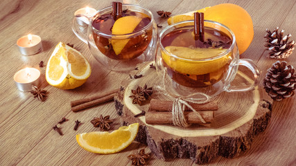 Orange flavored tea with cinnamon and cardamom in glasses, orange and cinnamon sticks lit by candlelight on a wooden table. Mulled wine and spices on wooden background. Selective focus. Close up.