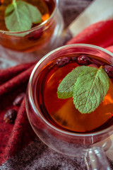 Dried rose-hip berries and rosehip tea on the rustic table. In a glass cups tea of rosehip and leaves mint. Medicinal plants and herbs composition. Autumn and winter season background. Close up