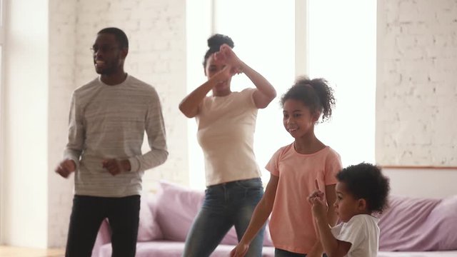 Happy african parents and cute funny kids dancing at home