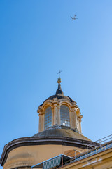 Fototapeta na wymiar Plane in blue sky fly over church on the street of Naples