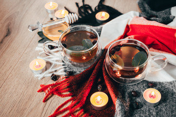 Black cup tea with dried rosehip and fresh leaves mint on the background of scattered dried rose hips and wax candles. Selective focus. Close up. Autumn and winter background.