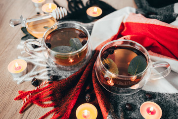 Black cup tea with dried rosehip and fresh leaves mint on the background of scattered dried rose hips and wax candles. Selective focus. Close up. Autumn and winter background.