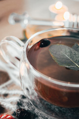 Black cup tea with dried rosehip and fresh leaves mint on the background of scattered dried rose hips and wax candles. Selective focus. Close up. Autumn and winter background.