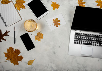 Workspace with autumn yellow leaves, laptop, tablet, smartphone, notebook and glass of wine. Top view of autumn freelancer working place.