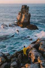 Traveler in the yellow jacket standing on the rocks in front of a huge waves © irengorbacheva