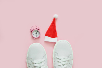 White women's sneakers, watch and Santa Claus hat on pink pastel background. The concept of the New Year, Christmas. Fitness concept. Copy space. Top view. flat lay.Fashion blog or magazine concept.