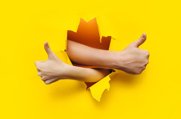 Like and like. Thumbs up sign of a man’s and woman hand. The wrist came out through the torn hole...