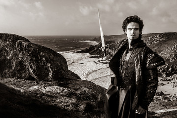 Black and white portrait of handsome knight holding sword and pointing to coastline in the distance