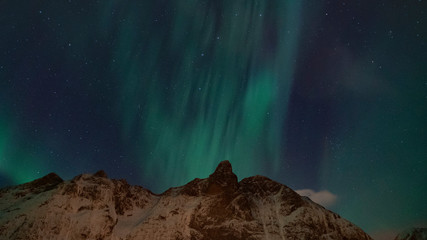 aurore bor&eacute;ale sort depuis l'arri&egrave;re d'une montagne pointue enneig&eacute;e