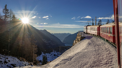 le train rouge glacier express traverse des paysages enneig&eacute;s au soleil en suisse