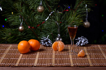 Fototapeta na wymiar A glass of cognac with tangerines on the surface of the table against the background of the Christmas tree.