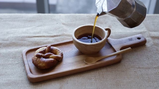 Pouring coffee in a wooden cup on the table.