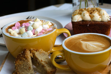 Two large brown cups of morning cappuccino and bebicino coffee with marshmallows and carrot cake on the table. Fragrant breakfast for two.