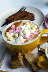 Two large brown cups of morning cappuccino and bebicino coffee with marshmallows and carrot cake on the table. Fragrant breakfast for two.
