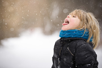 Adorable kid boy having fun in the park catching snowflakes with tongue. Funny child with blond...