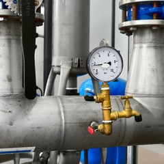 Large industrial water treatment and boiler room. Shiny steel metal pipes, switches and a barometer