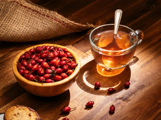 Wooden bowl full of rose hips and cup of tea