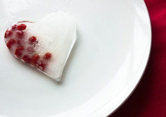 shape of ice heart  on white plate  over red background. Top view.
