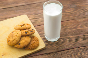 Chocolate chip cookies with milk in glass on rustic wooden table