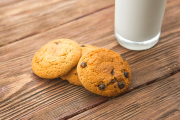 Chocolate chip cookies with milk in glass on rustic wooden table